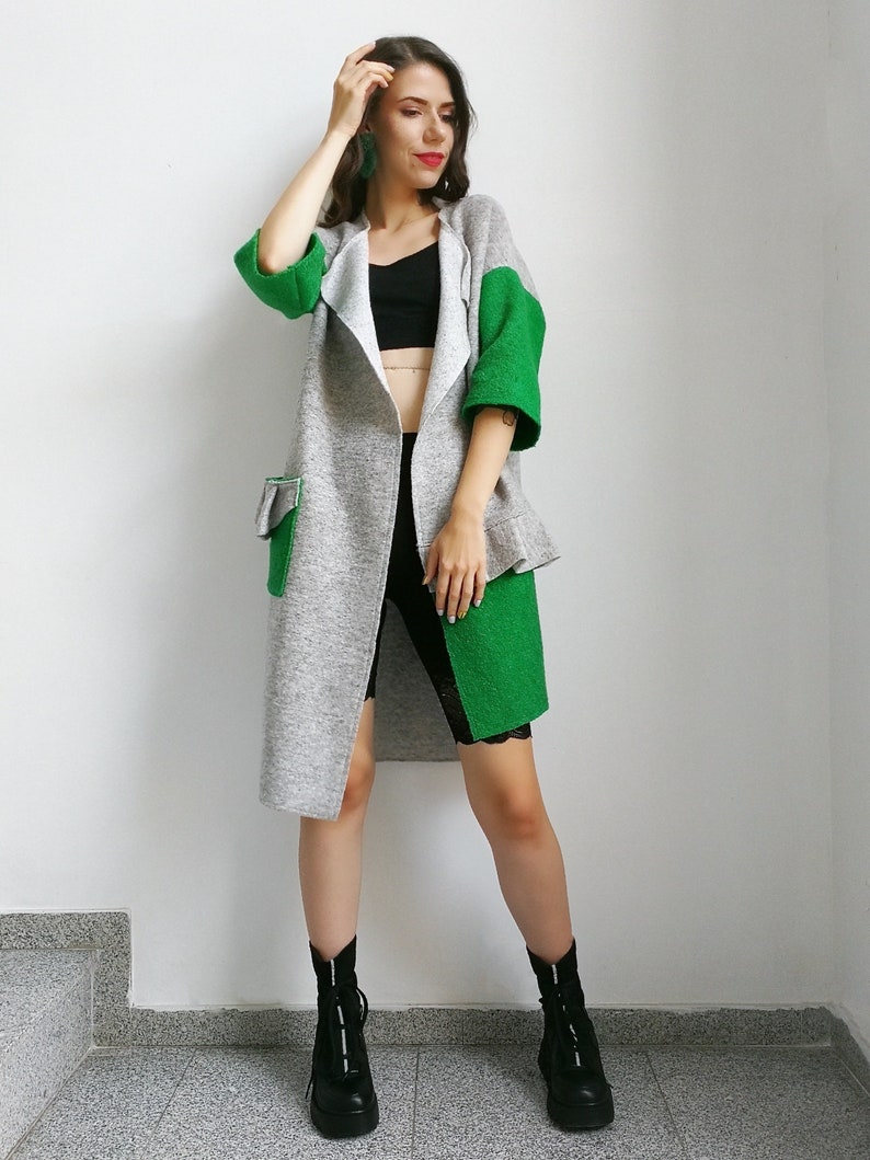 May include: A long gray and green cardigan with a black top and black biker shorts. The person is wearing black ankle boots.