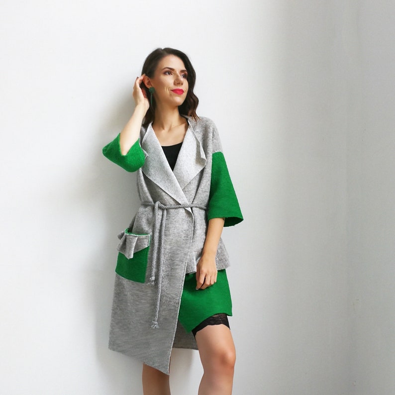 May include: A gray and green cardigan with a long, asymmetrical hemline. The cardigan has a tie belt and a large pocket on the left side.