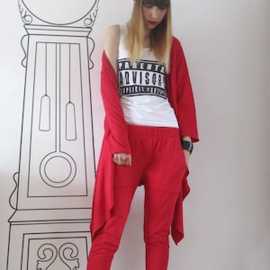 Peut inclure: Une femme portant un cardigan rouge, un pantalon rouge et des baskets blanches. Elle porte un d&eacute;bardeur blanc avec l'inscription "Parental Advisory Explicit Content". Elle porte &eacute;galement un bandana noir sur la t&ecirc;te.