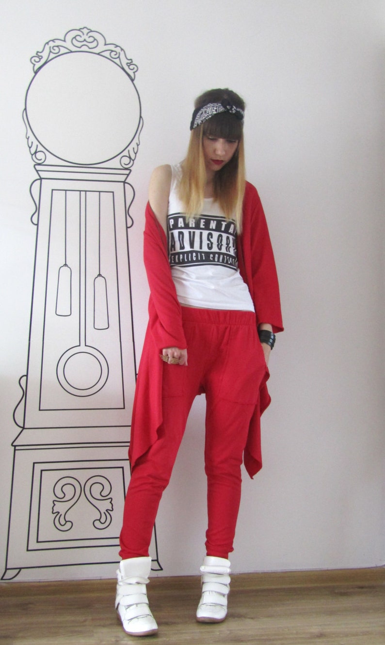 Peut inclure: Une femme portant un cardigan rouge, un pantalon rouge et des baskets blanches. Elle porte un d&eacute;bardeur blanc avec l'inscription "Parental Advisory Explicit Content". Elle porte &eacute;galement un bandana noir sur la t&ecirc;te.