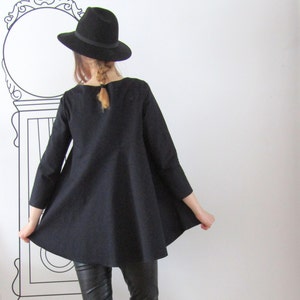 May include: A black, long-sleeved, A-line tunic with a scoop neck. The tunic is worn with black leather pants and a black fedora.