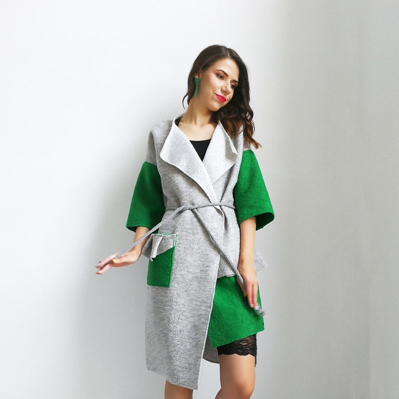 May include: A gray and green wrap coat with a long, flowing silhouette. The coat has a wide collar and a tie belt. The sleeves are three-quarter length and the coat is lined with a white fabric.