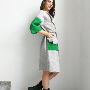 May include: A gray and green knitted dress with a ruffled pocket and a belt. The dress has long sleeves with green cuffs. The model is wearing black combat boots.