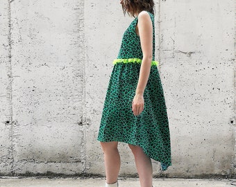 May include: A green dress with a leopard print and a lime green trim around the waist. The dress has a high low hemline and is being worn with white platform sneakers.