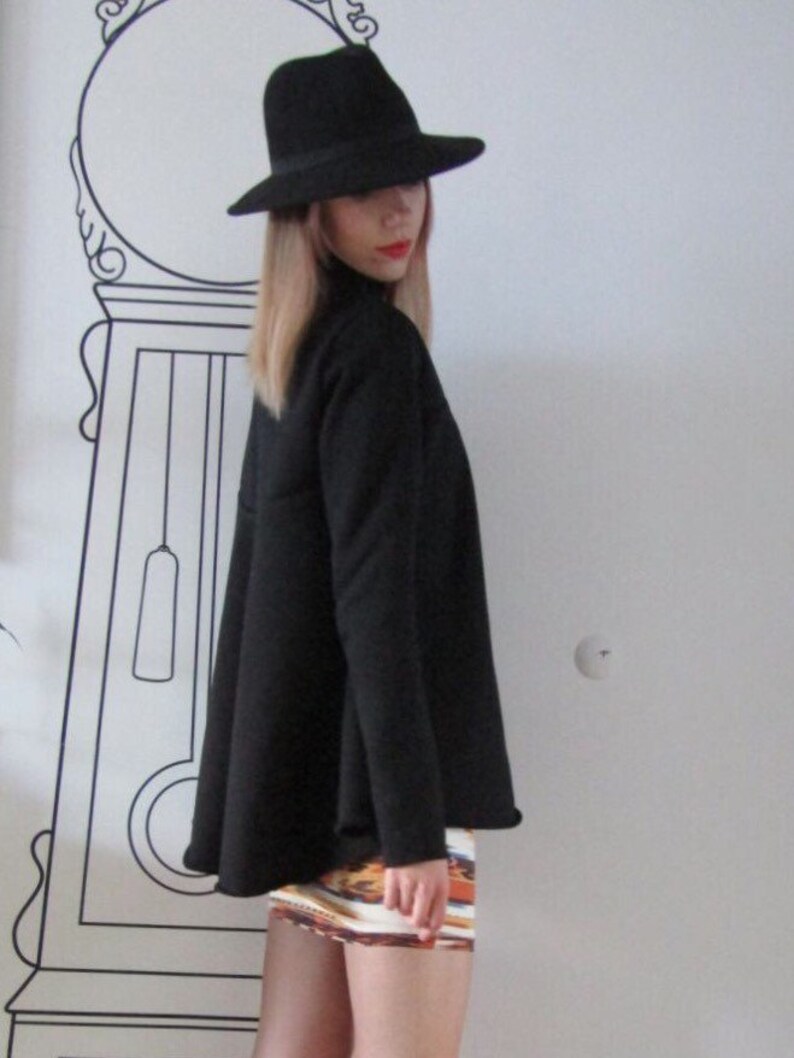 May include: A woman wearing a black fedora hat, a black long-sleeved shirt, and a colorful patterned mini skirt.