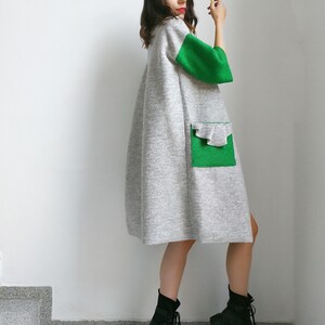 May include: A gray and green long-sleeved dress with a ruffled pocket. The dress has a loose fit and is made of a soft, comfortable fabric.