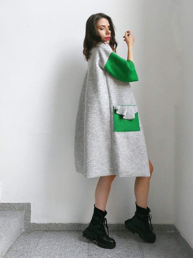 May include: A gray and green long-sleeved dress with a ruffled pocket. The dress has a loose fit and is made of a soft, comfortable fabric.