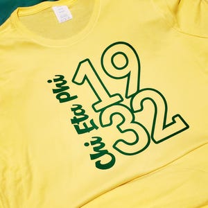 Può includere: T-shirt giallo con la scritta "Chi Eta Phi" e i numeri "1932" in verde. La maglietta è realizzata in materiale morbido e ha un girocollo.