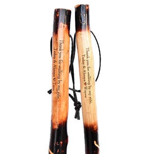 Pu&ograve; includere: Due bastoni da passeggio in legno con punte nere e messaggi incisi. I messaggi recitano "Grazie per aver camminato al mio fianco, Oggi e per sempre Wayne" e "Grazie per aver camminato al mio fianco, Oggi e per sempre Tara".