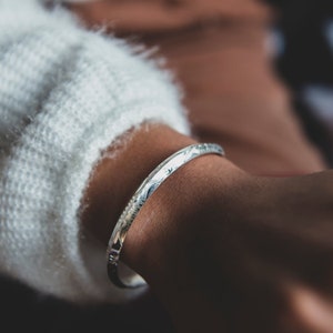 May include: A silver bangle bracelet with an intricate engraved design.