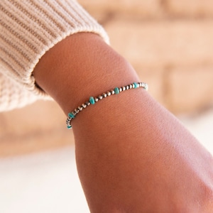 May include: A silver bracelet with turquoise beads. The bracelet is on a person's wrist.