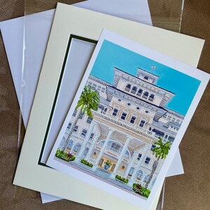 May include: A framed print of a watercolor painting depicting a large, white building with a blue sky and palm trees. The building has a large porch with columns and a sign that reads "Wiches".