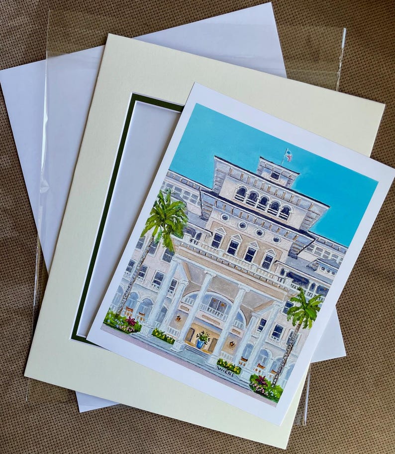 May include: A framed print of a watercolor painting depicting a large, white building with a blue sky and palm trees. The building has a large porch with columns and a sign that reads "Wiches".