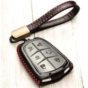 May include: Black leather key fob with red stitching and a metal loop. The fob has a keyless entry remote with multiple buttons.