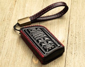 May include: Black leather key fob with red stitching and a metal loop. The fob has multiple buttons.