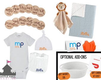 May include: A baby gift set with a white onesie, hat, and bib, all personalized with the name "Stella". The set also includes a blue and white muslin blanket, a lion-shaped security blanket, and a wooden set of monthly milestone markers. The set is presented on a white background with a castle logo and the text "Castle Hall Creative".