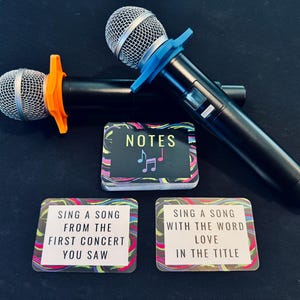 Two karaoke microphones with a card game next to them. The game is called Notes and there are two cards turned over that read "