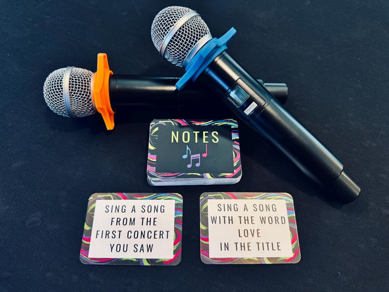 Two karaoke microphones with a card game next to them. The game is called Notes and there are two cards turned over that read "