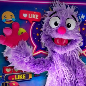 May include: A purple puppet with a pink nose and mouth, and large eyes, waves in front of a social media-themed backdrop. The background includes like icons, emojis, and a neon glow. The logo for "My Puppet Journey" is in the lower left.