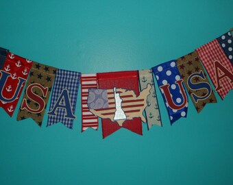 May include: A patriotic banner with the letters "USA" on various patterned flags. The flags include red, white, and blue designs with anchors, stars, and polka dots. A central flag features a map of the United States.