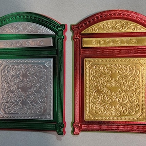 May include: Two decorative mailboxes, one green and silver, the other red and gold. Both have a rectangular shape with ornate scrollwork and the word "POST" on a horizontal bar. The mailboxes are likely for holiday decor.