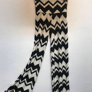 Op de afbeelding: Zwarte en witte broek met chevron-patroon hangend aan een hanger. De broek is wijd uitlopend en heeft een hoge taille.