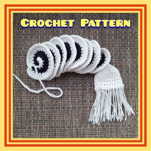 May include: A crochet pattern for a white and black crocheted flower with a white crocheted tassel. The pattern is called "CROCHET PATTERN".