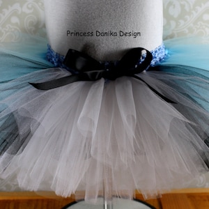 May include: A white, black, and light blue tulle tutu with a black ribbon and a blue crocheted waistband. The tutu is on a white mannequin.