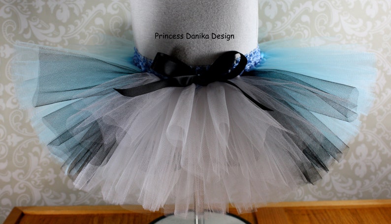 May include: A white, black, and light blue tulle tutu with a black ribbon and a blue crocheted waistband. The tutu is on a white mannequin.