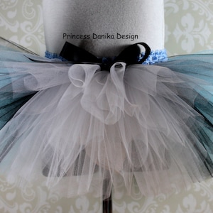 May include: A white, black, and light blue tulle tutu with a black ribbon and bow. The tutu is on a white mannequin. The text "Princess Danika Design" is on the ribbon.
