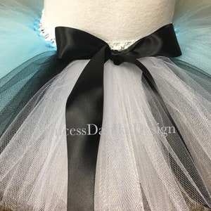 May include: A multi-layered tulle tutu skirt with a black satin ribbon tied in a bow at the waist. The skirt is layered in shades of blue, black, and white.