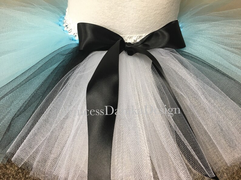May include: A multi-layered tulle tutu skirt with a black satin ribbon tied in a bow at the waist. The skirt is layered in shades of blue, black, and white.