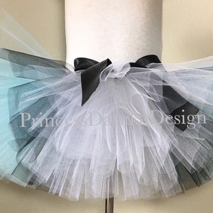 May include: A multi-layered tulle tutu skirt with a black satin bow. The skirt is ombre, starting with light blue, then black, and finally white.