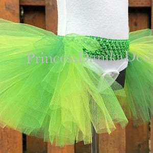 May include: A green and yellow ombre tulle tutu with a green crocheted waistband. The tutu is layered and full, creating a fluffy and whimsical look.