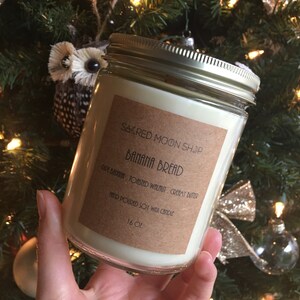 Könnte beinhalten: Eine Glaskerze in einem Einmachglas mit einem braunen Etikett, auf dem "SACRED MOON SHOP BANANA BREAD RIPE BANANA, TOASTED WALNUT, CREAMY BUTTER HAND POURED SOY WAX CANDLE 16 OZ" steht.