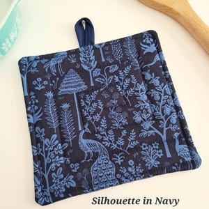 Puede incluir: Manopla acolchada azul marino con un dise&ntilde;o de silueta azul de &aacute;rboles, plantas y pavos reales. Tiene un lazo azul marino para colgar y el texto "Silhouette in Navy".