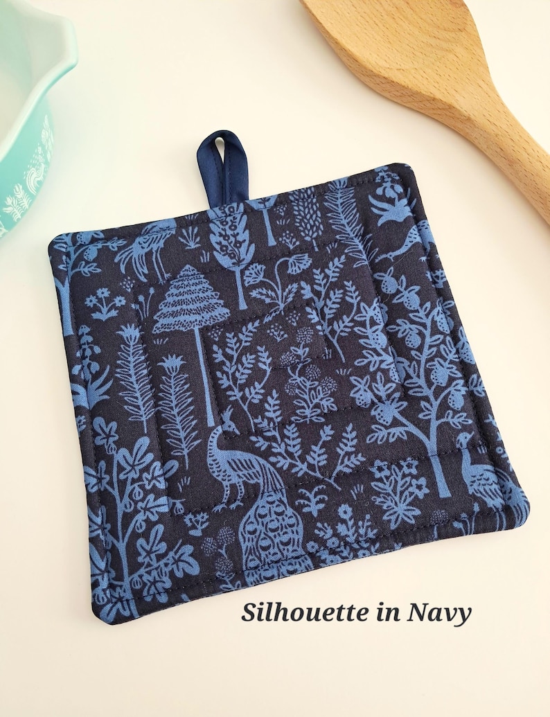 Puede incluir: Manopla acolchada azul marino con un dise&ntilde;o de silueta azul de &aacute;rboles, plantas y pavos reales. Tiene un lazo azul marino para colgar y el texto "Silhouette in Navy".