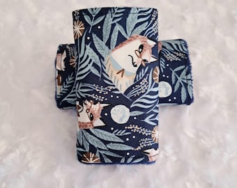 May include: Four navy blue fabric drink sleeves with a whimsical forest pattern featuring hedgehogs, leaves, and floral accents. The sleeves are designed to keep beverages cold and hands dry. The fabric has a soft, textured feel.