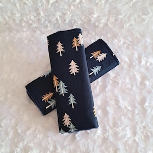 May include: Two navy blue seatbelt covers with a repeating pattern of stylized trees in white, gold, and light blue. The covers are made of a soft fabric and are designed to protect the wearer from seatbelt chafing.