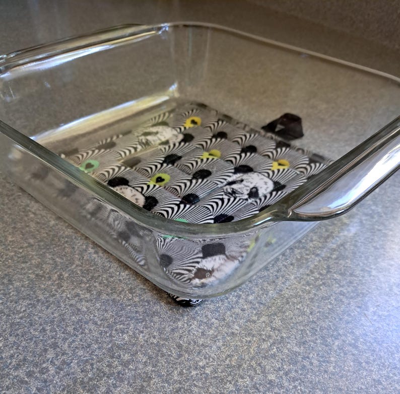 Puede incluir: Una fuente de horno de vidrio transparente con un cuadrado de tela estampada en el interior. La tela presenta un dise&ntilde;o de rayas de cebra en blanco y negro con acentos amarillos y verdes. La fuente es rectangular con esquinas redondeadas.