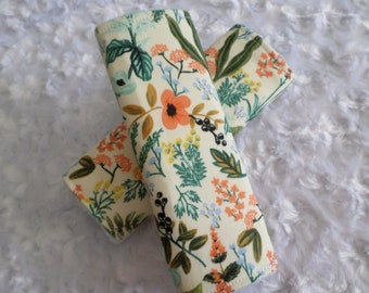 May include: Two fabric items with a floral pattern featuring orange, teal, and yellow flowers, green leaves, and black berries on a cream background. The items are likely accessories, possibly for a baby or child.