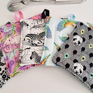 May include: A collection of colorful, patterned pot holders. Designs include black and white floral, pink elephant, zebra, parrots, and a black and white fan pattern with panda faces. Each pot holder has a loop for hanging.