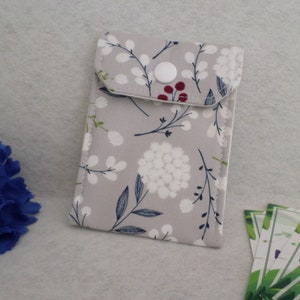 May include: A rectangular, floral-patterned pouch with a button closure. The pouch features a light gray background with white, navy, and burgundy floral designs. The pouch is likely used for carrying small items.