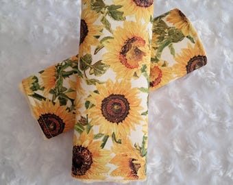 May include: Two fabric items with a sunflower pattern. The design features large yellow sunflowers with brown centers and green leaves on a cream background. The items are likely accessories or home decor.