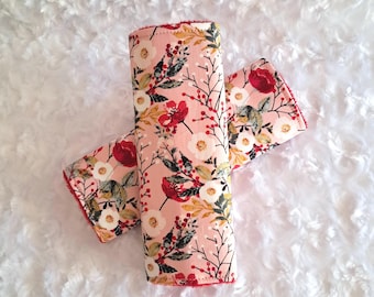 May include: Two floral print fabric items with a pink background, red trim, and a pattern of red, white, and green flowers and leaves. The items are rolled up and crossed over each other.