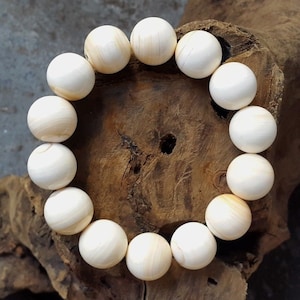 Puede incluir: Un brazalete blanco hecho de cuentas redondas con un patrón de veta de madera natural.