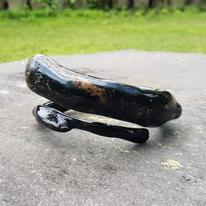 May include: A black, glossy, handcrafted bracelet with a unique, organic shape. The bracelet appears to be made of a dark material, possibly wood or a similar substance, and has a smooth, polished finish. The design is a spiral or wrap-around style.