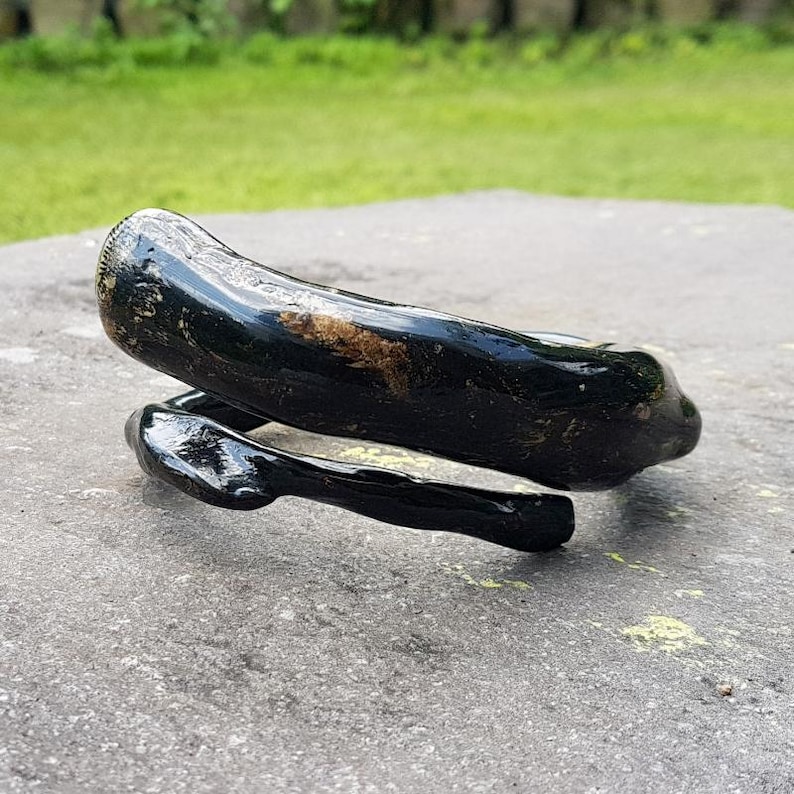 May include: A black, glossy, handcrafted bracelet with a unique, organic shape. The bracelet appears to be made of a dark material, possibly wood or a similar substance, and has a smooth, polished finish. The design is a spiral or wrap-around style.