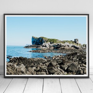 Può includere: Stampa incorniciata di un paesaggio costiero con una costa rocciosa e un'isola con una struttura in pietra. Il cielo è azzurro e l'acqua è blu scuro. L'isola ha vegetazione verde.