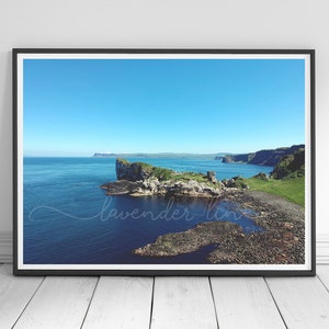 Può includere: Una fotografia panoramica di un'isola rocciosa con erba verde e cielo blu. L'isola è circondata da un'area d'acqua di colore blu scuro. L'acqua è calma e riflette il cielo. L'immagine è stata scattata da un punto di vista elevato, offrendo una vista ampia del paesaggio.
